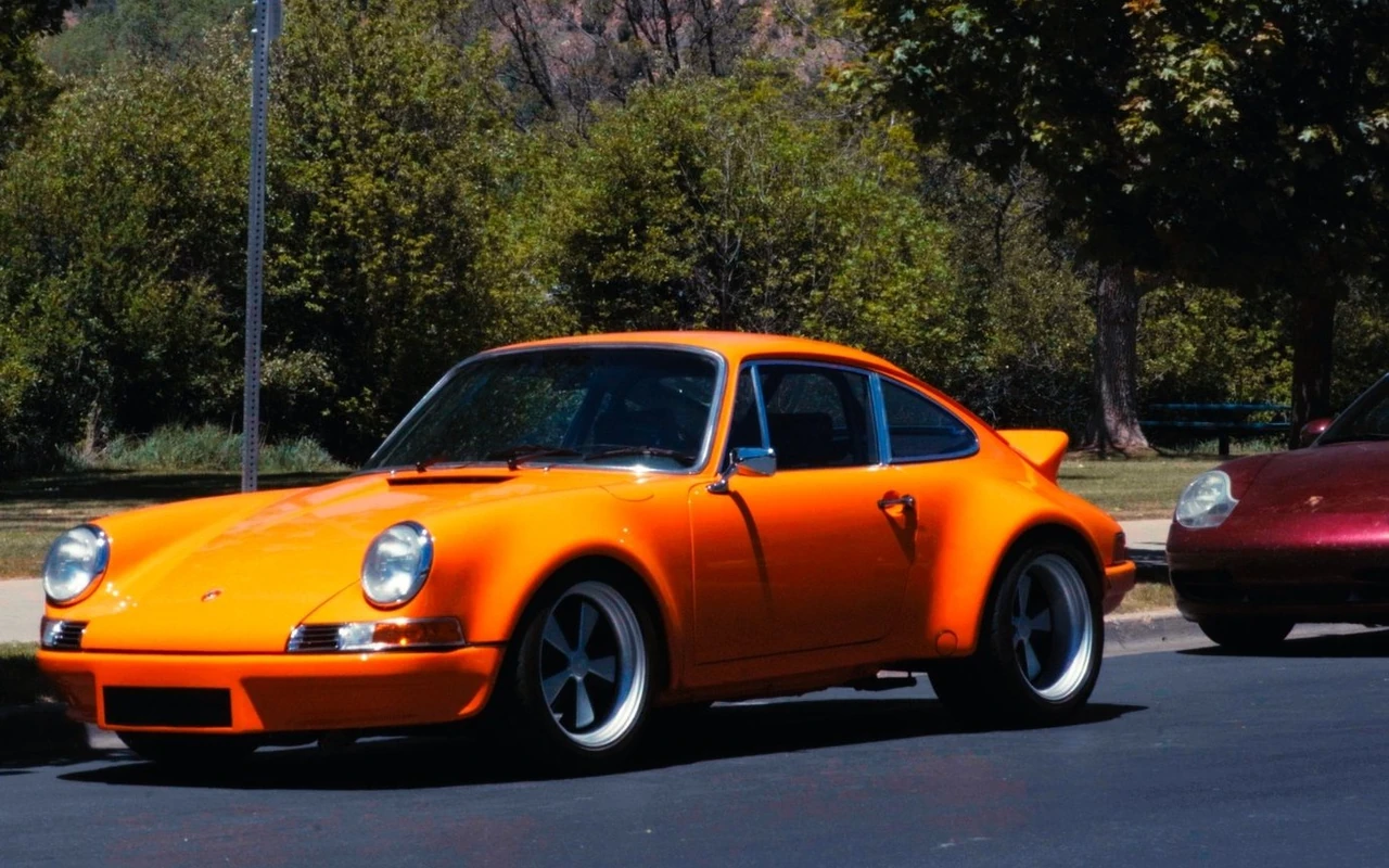 An orange 911 parked under trees