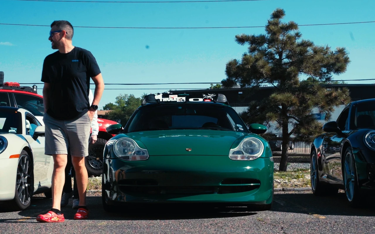 A green 911 in a lot with a driver standing beside it
